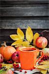 Orange mug on autumn background -fall leaves, apples, pumpkin and rowan-berry