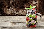Detox drink with fresh berries, mint and ice in glass jars on wooden background