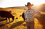 Portrait of farmer standing on a field with cows in the background.