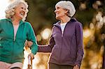 Smiling adult woman helping her friend to walk with a walking frame in a park.