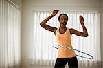 Portrait of a happy young woman hula hooping in her living room.