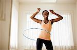 Happy young woman hula hooping in her living room.