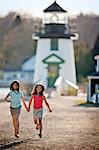 Young sisters running in front of lighthouse.