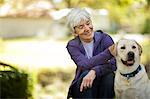 Smiling senior woman petting her dog in her garden.