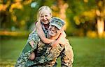 Portrait of a smiling army soldier giving his young daughter a piggy back in their back yard.