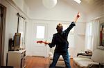 Mature man playing an electric guitar inside his sitting room.