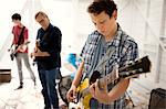 Two teenage boys and a man concentrating as they play their electric guitars.