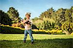 Young boy wears a pilot hat while playing with his toy plane in the garden.