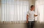 Teenage boy standing and looking out a window.