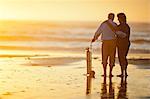 Female nurse comforting a senior male patient standing with his oxygen tank on a beach at sunset.