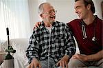 Cheerful elderly man with a nasal tube speaking with a male nurse at his hospital bed.