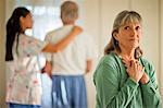 Senior woman looking hopeful while a nurse comforts her unwell husband.