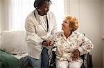 Smiling female doctor having a conversation with an elderly female patient sitting in a wheelchair.