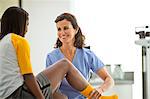 Smiling female doctor holding the injured leg of a teenage girl while sitting together inside a doctor's office.