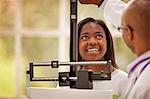 Smiling teenage girl having her height measured by a male doctor.
