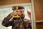 Mid adult man concentrating as he holds an electric drill while mending a door frame.