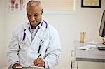 Focused male doctor taking notes on a clipboard inside his office.