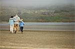 Senior couple walking on a beach with their young grandson.