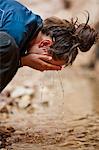 Young woman splashing water from a stream onto her face.