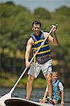 Smiling middle aged man paddle boarding with his son.