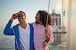 Happy young couple having fun with binoculars while sailing.
