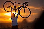 Smiling mature woman holding a bike above her head.