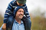 Smiling middle aged man carrying his young son on his shoulders.