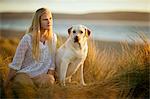 Teenage girl sitting in a grassy sand dune with her dog.