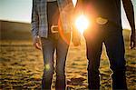 Farmer and his wife holding hands and walking through the fields of their ranch at sunset.