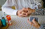 Elderly wife gently places her hand atop her husband's hands as they play cards together at the kitchen table.