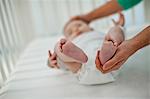 Young mother gently cups her baby boy's tiny foot after laying him gently in his cot.