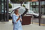 Beautiful woman holding umbrella while using mobile phone during rainy season