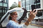 Beautiful woman holding umbrella while taking selfie during rainy season