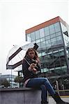 Beautiful woman holding an umbrella and using mobile phone on street