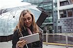 Beautiful woman holding an umbrella and using digital tablet on street