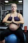 Pregnant woman performing yoga on fitness ball at gym