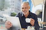 Smiling businessman using digital tablet drinking coffee at urban sidewalk cafe