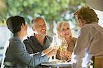 Couples toasting white wine glasses at sunny restaurant table