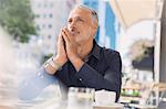 Pensive man drinking coffee at urban sidewalk cafe