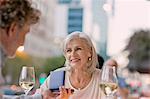 Smiling senior woman receiving jewelry gift from husband at urban sidewalk cafe