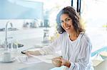 Portrait smiling businesswoman in bathrobe reviewing paperwork in kitchen