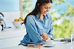 Smiling woman working reviewing paperwork at kitchen counter