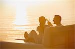 Silhouette couple toasting wine glasses on lounge chair with sunset ocean view