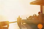 Silhouette woman using cell phone on chaise lounge on luxury balcony with sunset ocean view