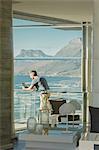 Reflection of man using digital tablet on luxury balcony with ocean and mountain view