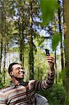 Smiling man taking selfie with camera phone in sunny woods