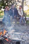 Friends watching fish cooking in grill basket on campfire