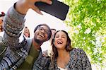 Enthusiastic friends taking selfie with camera phone below tree