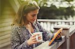 Woman drinking coffee and using digital tablet on balcony