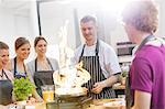 Students watching teacher flambe in cooking class kitchen